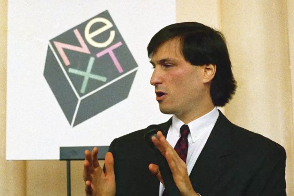 Steve Jobs in front of the NeXT logo