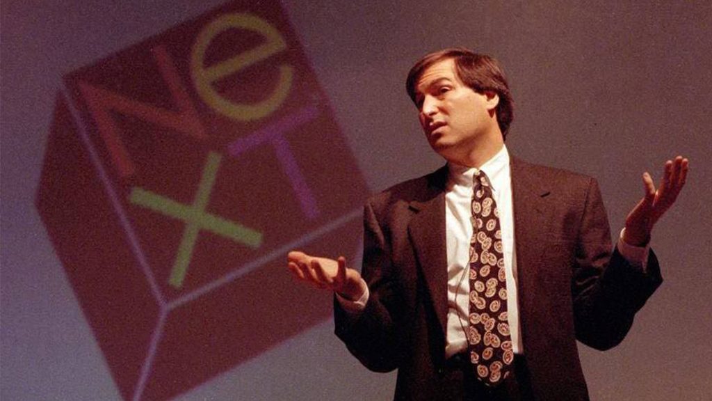 Steve Jobs in front of the NeXT logo